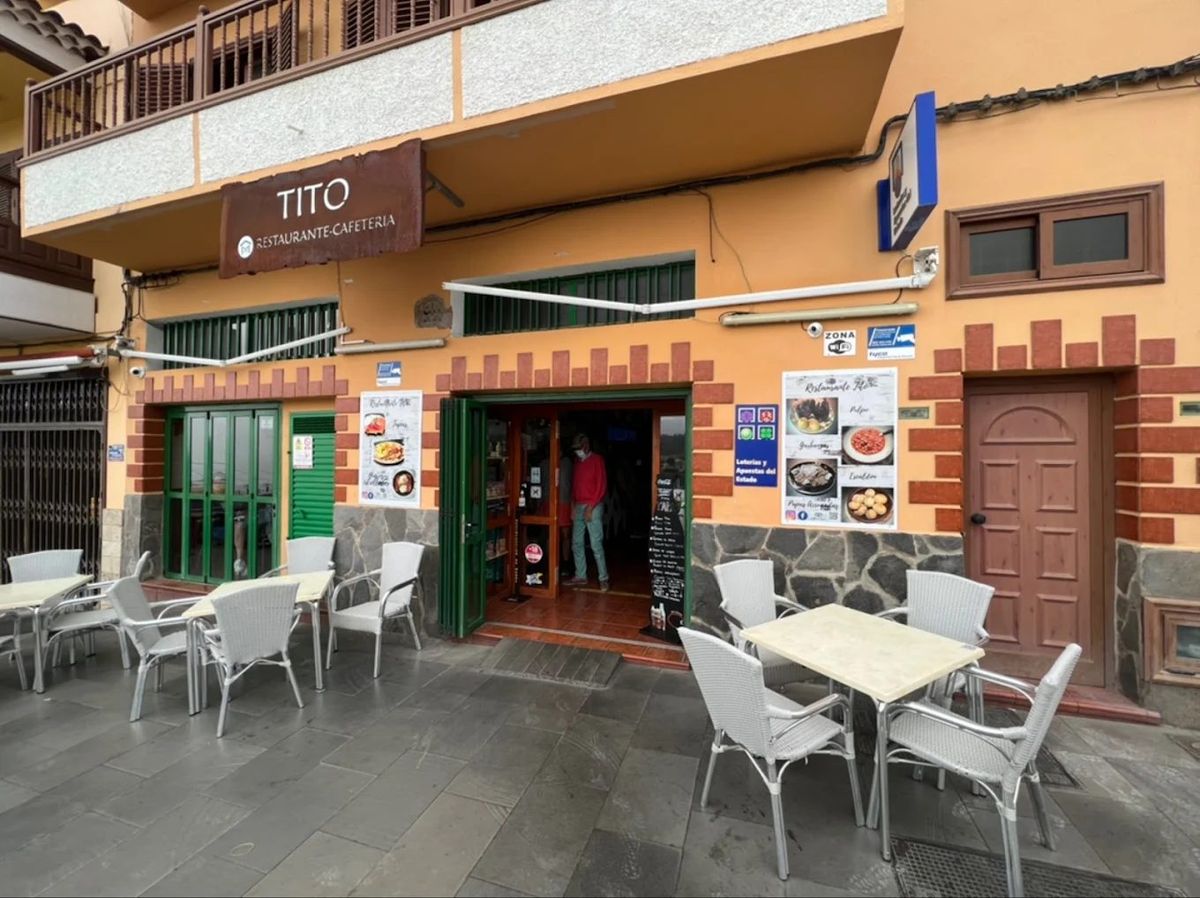 The front of Restaurante Cafetería Tito: the brown TITO sign above the open green doors, menu posters on the orange wall and white chairs on the terrace