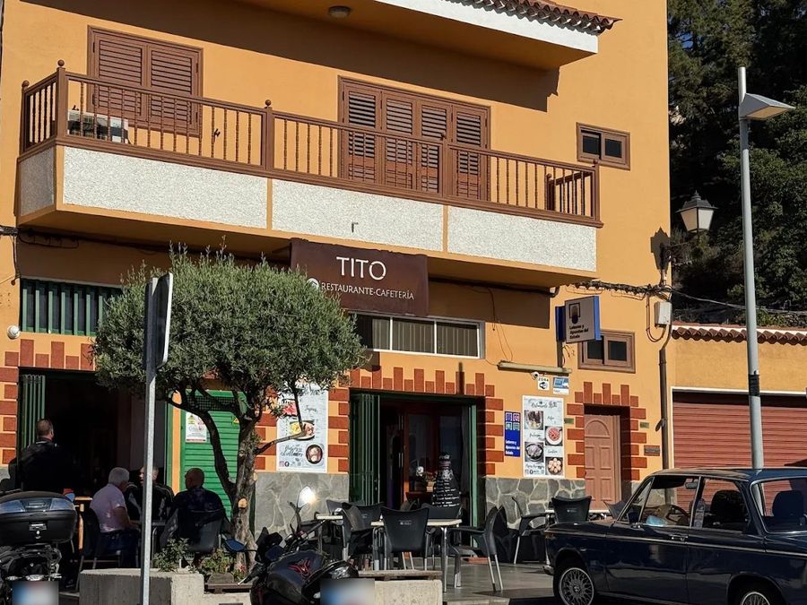 Motorbikes parked in front of the orange house with the brown TITO sign, guests sitting on the terrace